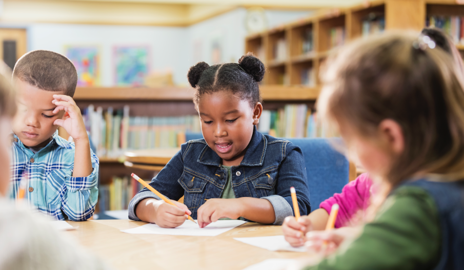 several elementary-age childred at a table at school writing with pencils